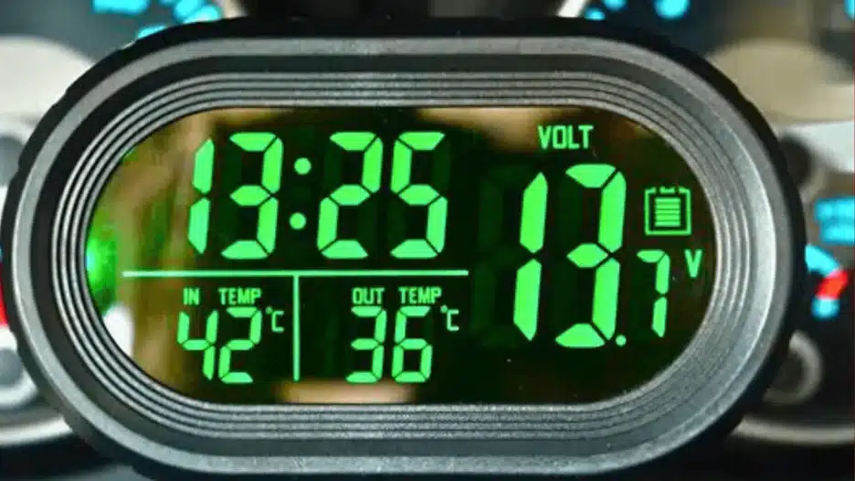 A close-up of a digital clock with thermometer and voltage display, showing the time (13:25), current battery voltage (13.7V with a battery icon), interior temperature (42°C), and exterior temperature (36°C) in green segmented digits.