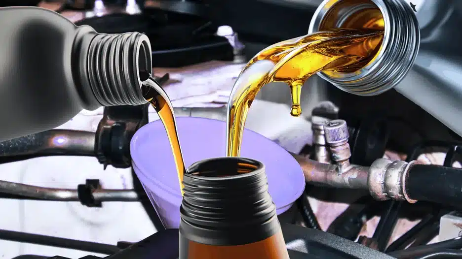 Engine oil being poured from two bottles into a funnel inside a car engine bay during an oil fill or oil change process.