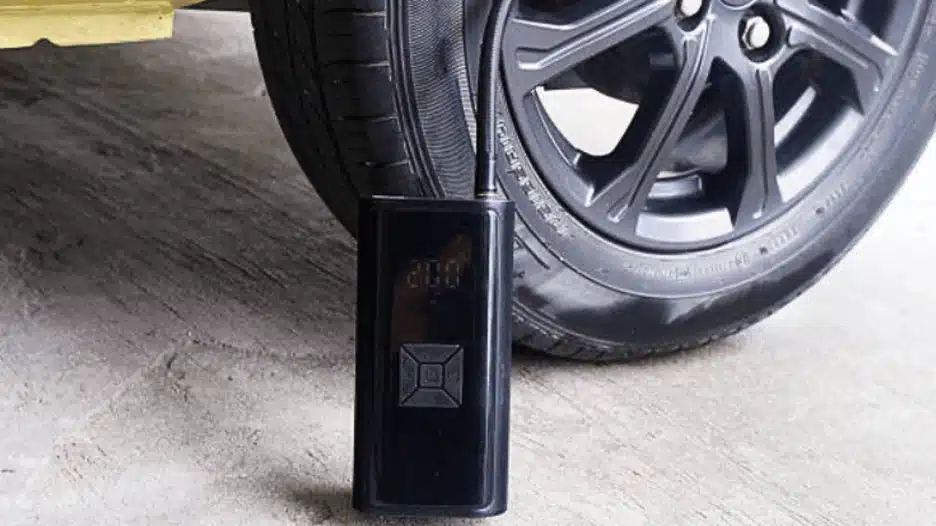 Portable tire inflator pump connected to a car tire, inflating the wheel on a concrete floor with a compact air compressor device.