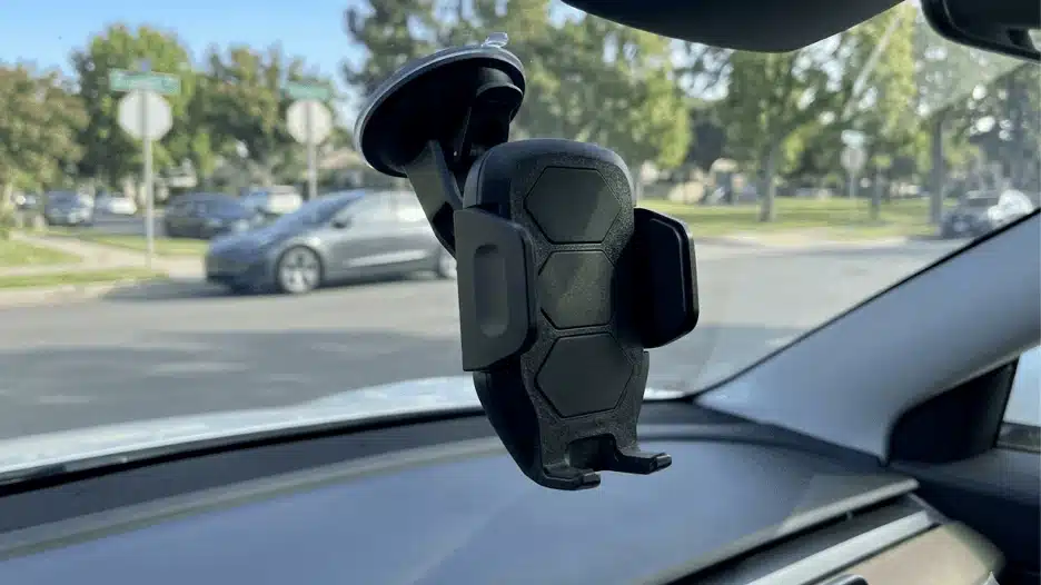 dashboard car phone holder mounted on windshield holding smartphone securely for hands free navigation while driving on a city street.