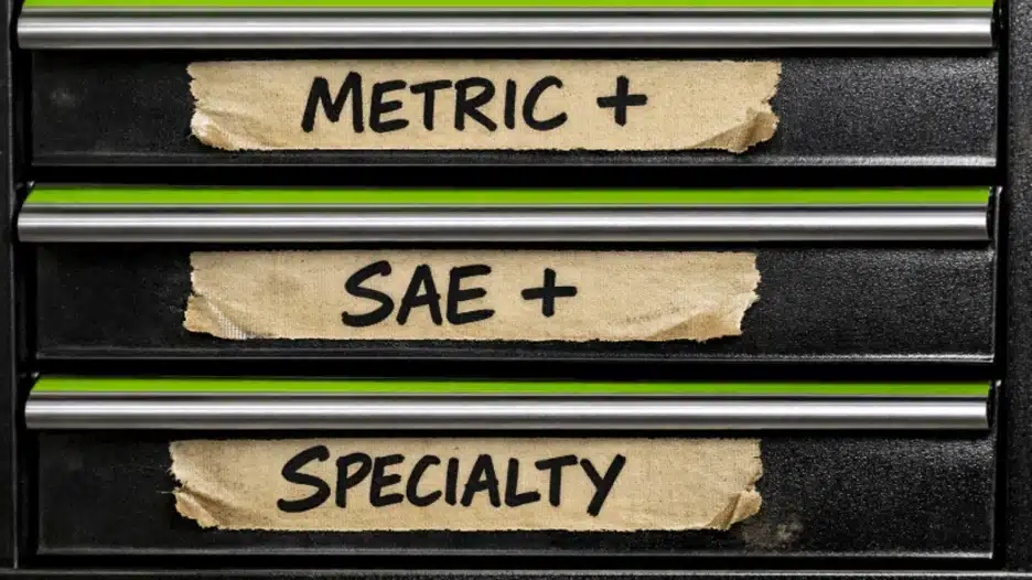 Close-up of three stacked black toolbox drawers with neon green trim lines and tan masking-tape labels handwritten in black marker reading “METRIC +,” “SAE +,” and “SPECIALTY.”