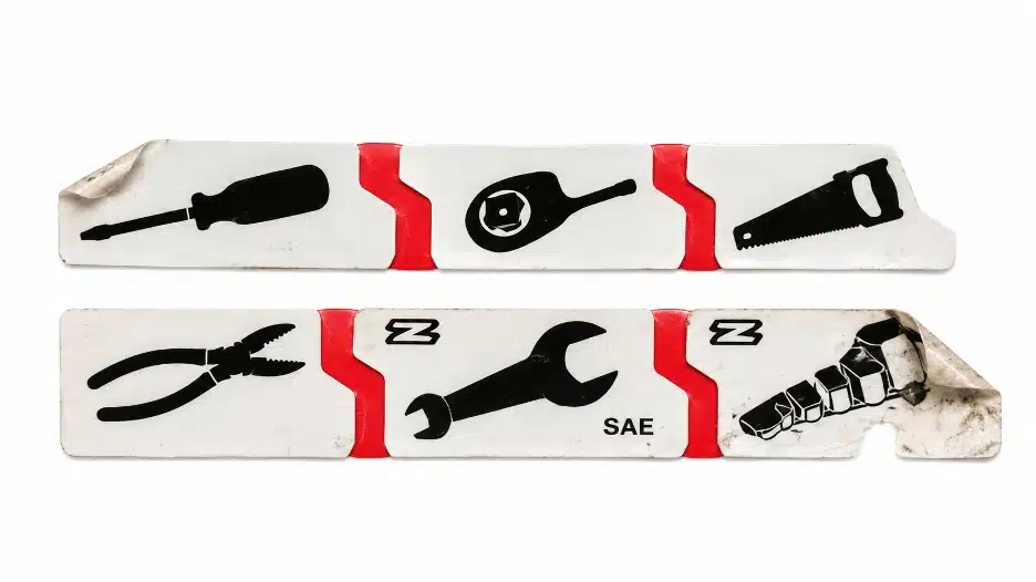 Close-up of worn adhesive toolbox sticker labels with printed tool icons, showing peeling edges, dirt buildup, and everyday wear from repeated use.