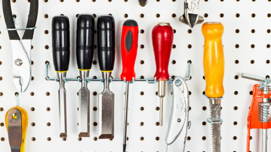 Garage pegboard tool storage with screwdrivers, pliers, clamps, and other hand tools arranged on a white perforated wall panel.